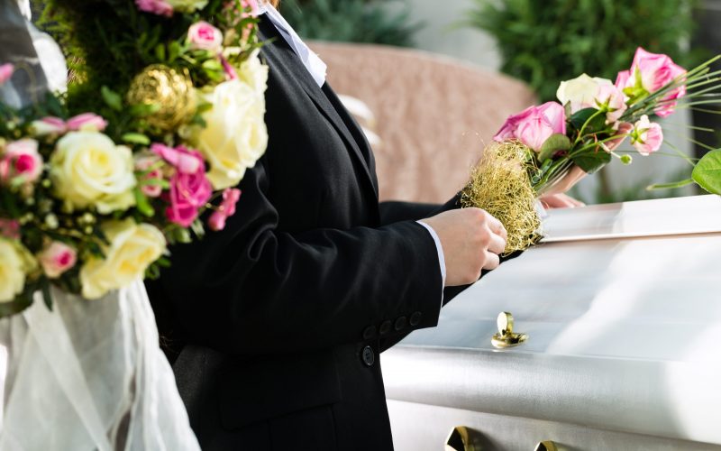 Mourning People at Funeral with coffin Mourning man and woman on funeral with pink rose standing at casket or coffin